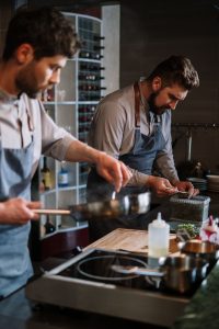 Two male chefs preparing dishes in a professional open kitchen setting.